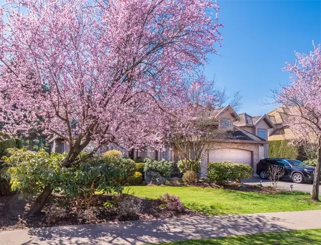 Beautiful home with blooming spring trees and green lawn, representing the ideal season to improve insulation and home comfort